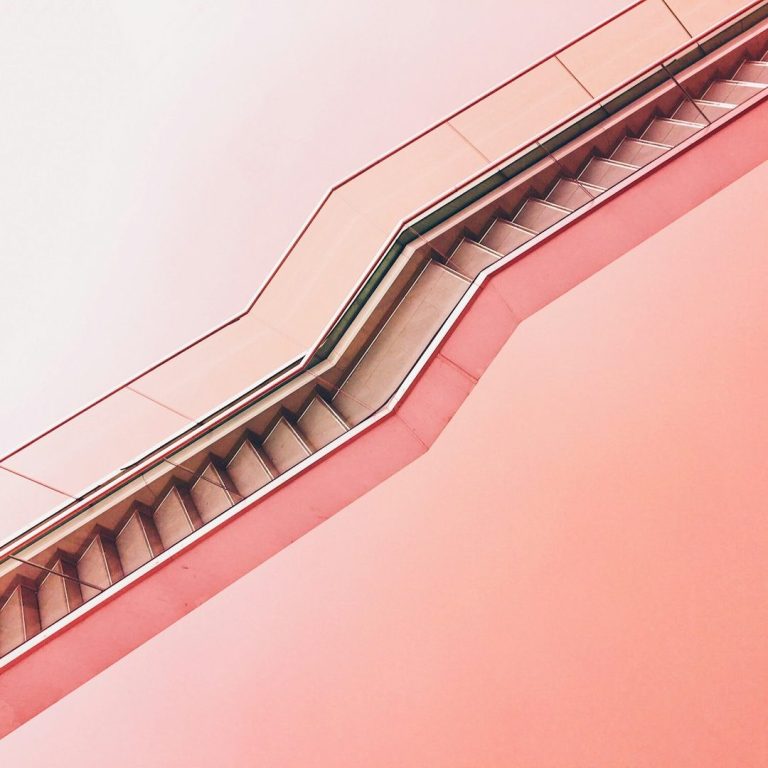 Treppenaufgang mit geschwungenem Geländer vor einem rosafarbenen Hintergrund.